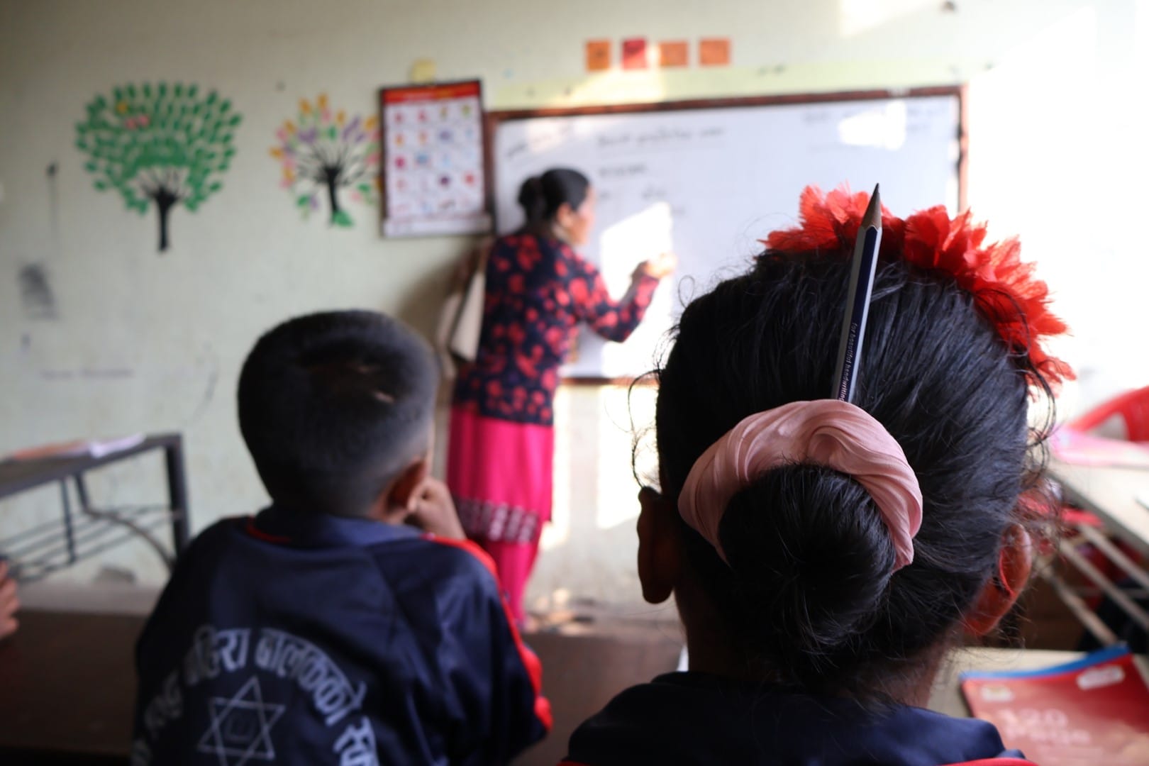 A teacher writing on a whiteboard as two students watch and listen.