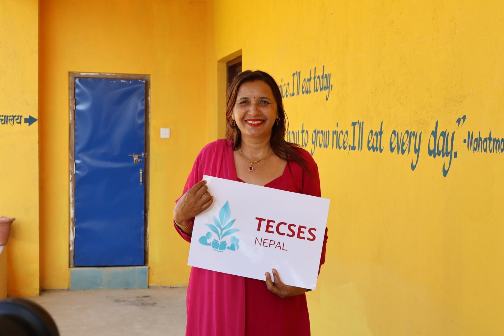 A teacher holding a TECSES sign and smiling.