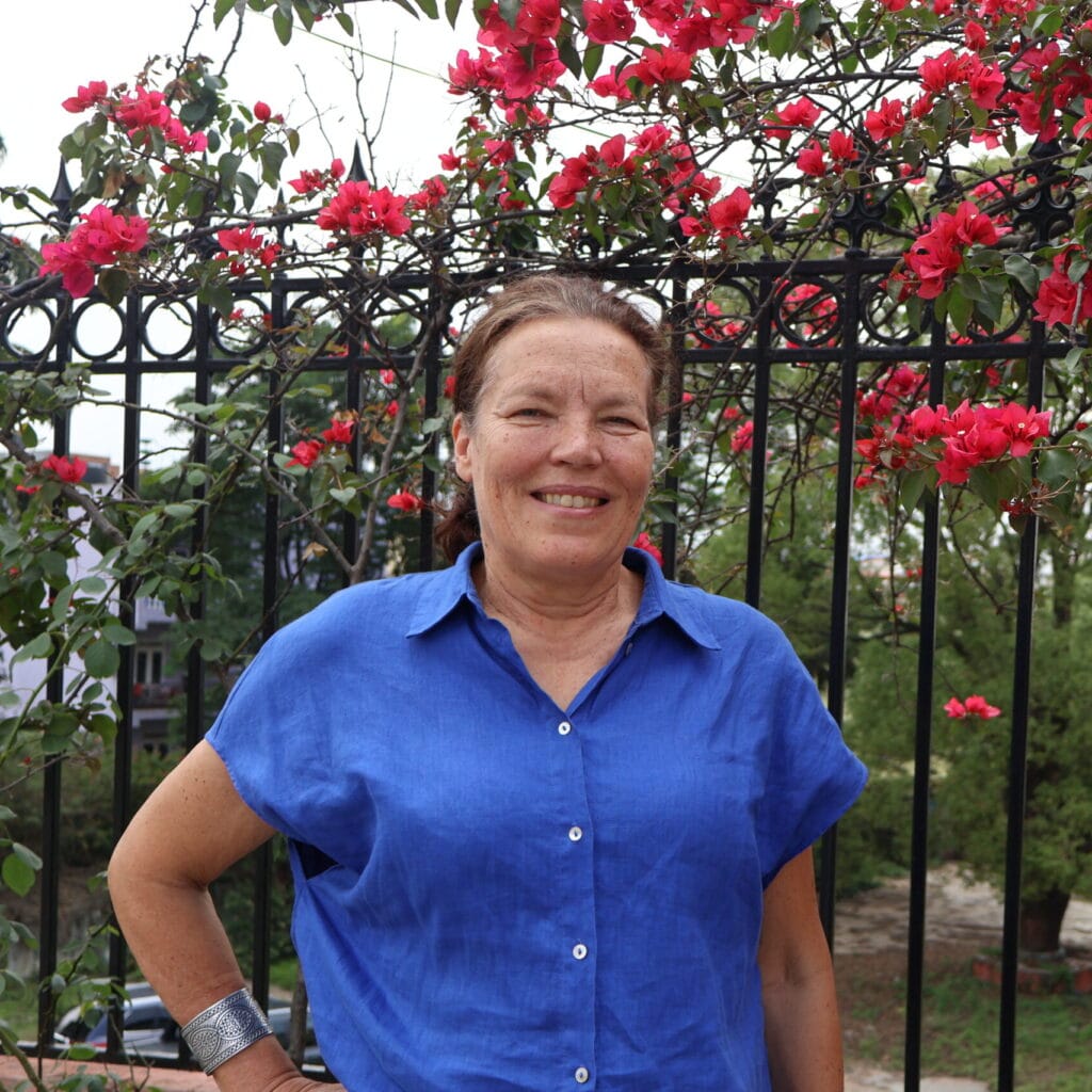 Eija-Riitta Kinnunen standing in front of pink flowers.