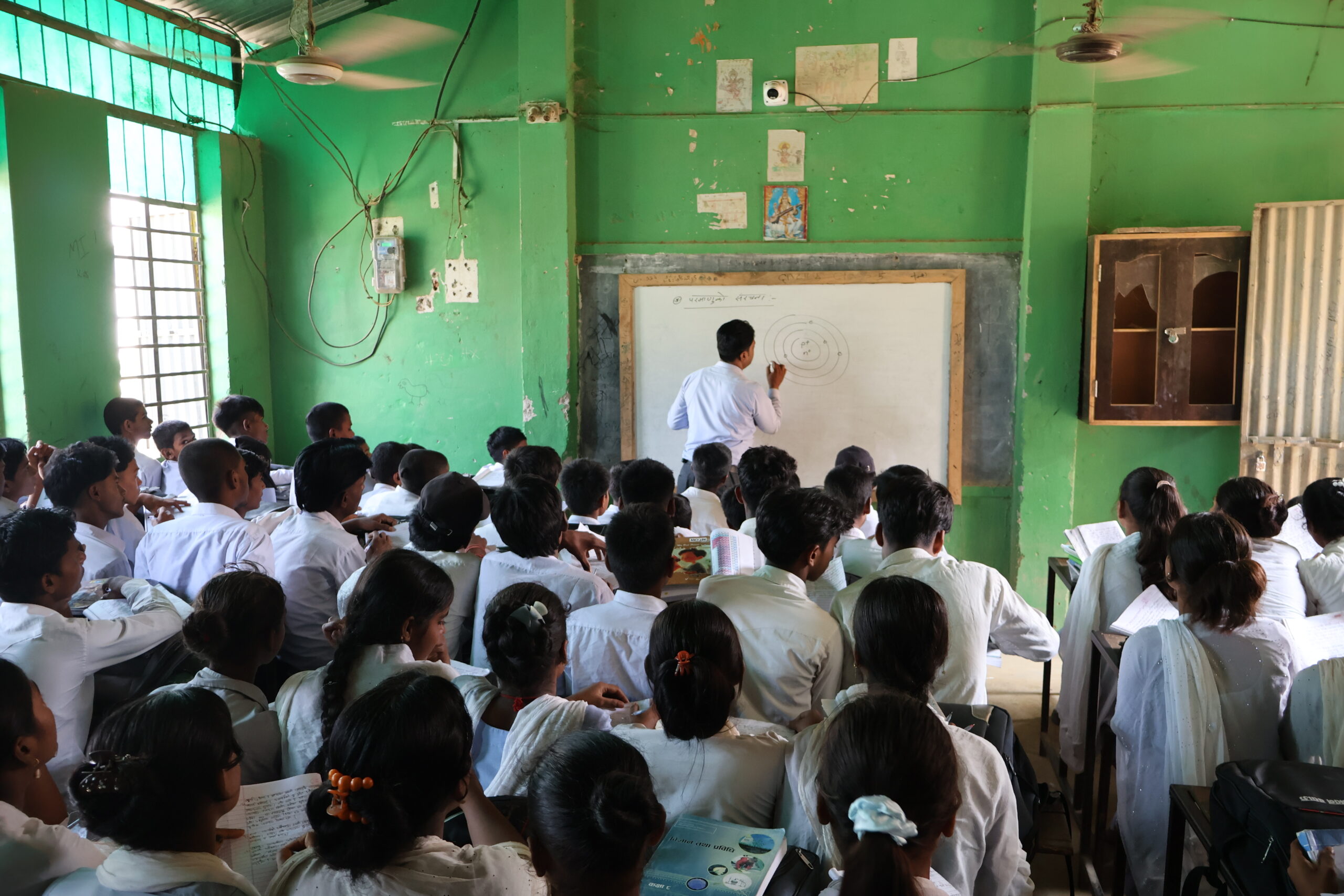 Teacher teaching a class full on Nepali children and writing on a white board